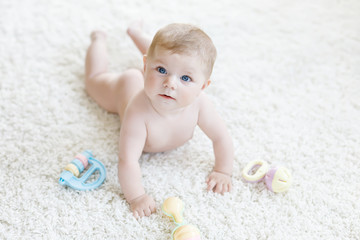 Cute baby playing with colorful pastel vintage rattle toy. New born child, little girl looking at the camera and crawling. Family, new life, childhood, beginning concept. Baby learning grab.