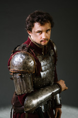 Medieval man knight in armor and weapon on dark background. Portrait of the knight