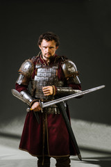 Medieval man knight in armor and weapon on dark background. Portrait of the knight