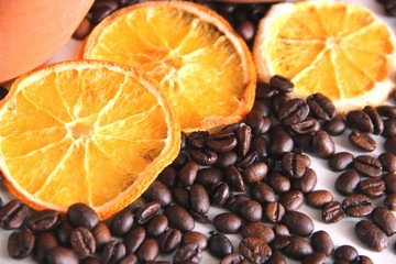 three pieces of dried orange and many roasted coffee beans on the table on the background of clay dishes, close-up