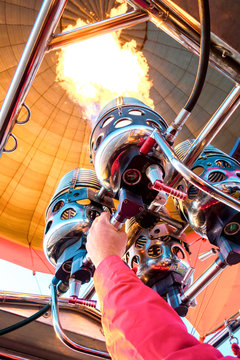 Hot air balloon flight. Close up view inside the dome of aerostat. Hand of pilot or captain holding gas-burner from which the flame escapes.