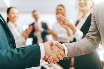 Close up of two partners shaking hands while other colleagues clapping hands. Be a boss, build an...