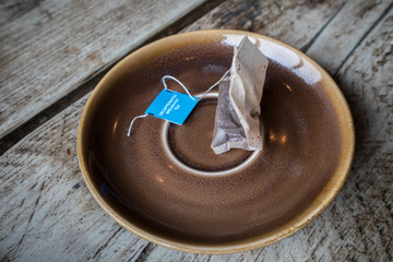 Used Decaffenated Tea Bag on a earthen ware saucer and rustic wooden table