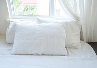 White sheets, blanket and pillows on the cozy bed with a window at the back. Bedding concept.