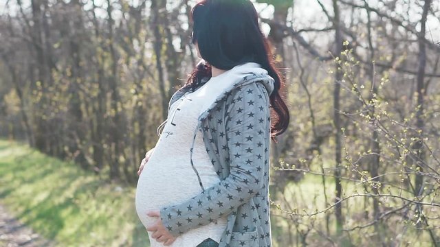 Young pregnant woman enjoying the beautiful weather in the forest. Happy pregnant woman is thinking about future motherhood. Woman at 36 weeks gestation (9 month).