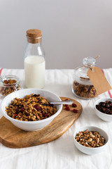 Bowl of homemade granola with nuts and fruits, bottle of milk on white linen background. Side view, copy space. Healthy breakfast concept