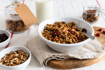 Bowl of homemade granola with nuts and fruits on white linen background. Side view