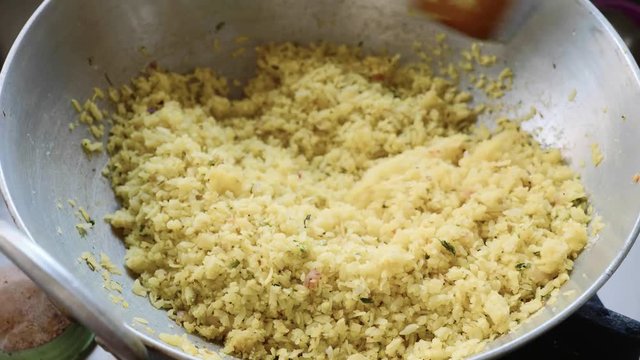 Close-up hand mixing traditional Indian dish poha in aluminum wok pan with wooden spatula.