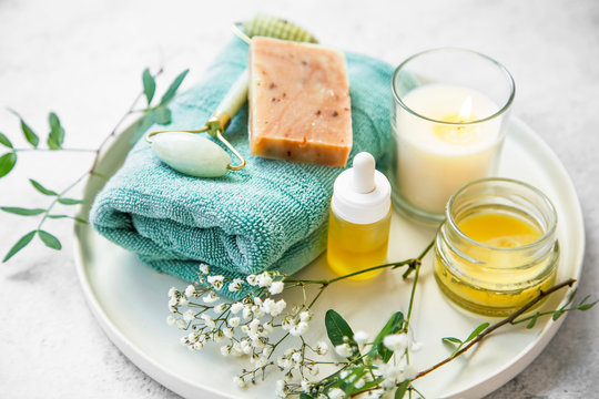 Natural organic skincare cosmetic products tray with natural soap, balm, oil, jade roller, candle and flowers, natural green skincare and spa products
