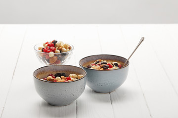 bowls with muesli, dried berries and nuts served for breakfast on white table isolated on grey