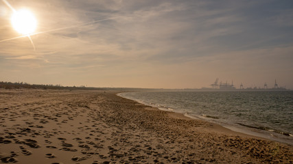 Long empty clean sand Stogi beach in Gdansk, Poland with DCT terminal. - obrazy, fototapety, plakaty