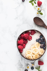 Healthy breakfast bowl. Banana smoothie bowl with coconut flakes, banana slices, raspberry and blueberry. Top view, flat lay