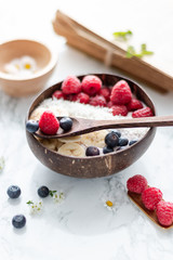 Healthy breakfast bowl. Banana smoothie bowl with coconut flakes, banana slices, raspberry and blueberry. Top view,
