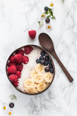 Healthy breakfast bowl. Banana smoothie bowl with coconut flakes, banana slices, raspberry and blueberry. Top view, flat lay