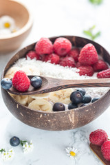 Healthy breakfast bowl. Banana smoothie bowl with coconut flakes, banana slices, raspberry and blueberry.  close up. wirh wooden spoon