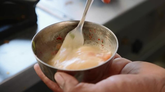 Cook mixes eggs and condiment with a fork in a small metal bowl prepares a masala omelette. And then pours the mass into the pan. Hands close-up.