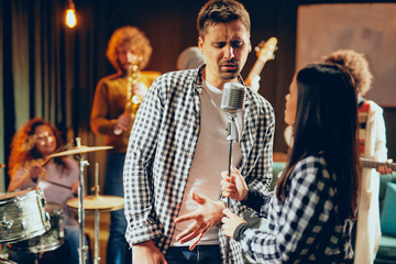 Singers practicing for duet. In background band playing. Home studio interior.