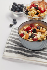 bowl on striped napkin with oat flakes, nuts and berries on white table