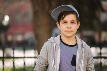 Stylish little school boy in blue cap posing outside for photo. Boy walking in the city in sping summer weather