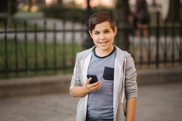 Front view of laughing teenage boy stand in the city with smartphone