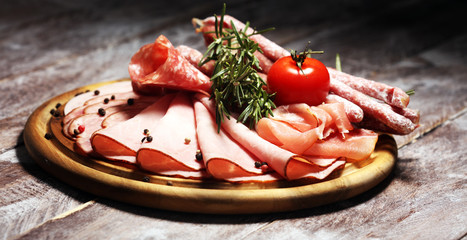 Food tray with delicious salami, pieces of sliced ham, sausage and salad. Meat platter selection.