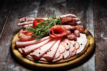 Food tray with delicious salami, pieces of sliced ham, sausage and salad. Meat platter selection.