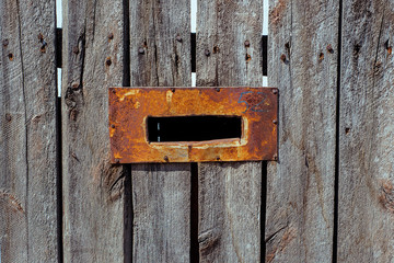 Mail hole with steel rusted frame on the wooden fence.