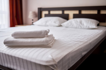 Fototapeta na wymiar Stack of white clean bath towels on bed sheet in modern hotel bedroom interior, copy space