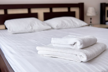 Stack of white terry bath towels on bed sheet in modern hotel bedroom interior, copy space