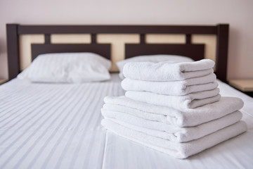 Fototapeta na wymiar Stack of white fresh bath towels on bed sheet in modern hotel bedroom interior, copy space