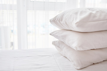 Stack of white soft pillows on comfortable bed sheet with window on background, copy space