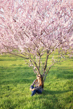 Young woman sitting under a blossom tree.