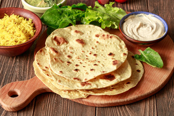 Indian vegetarian chapati cakes with vegetables, rice and hummus on a wooden table