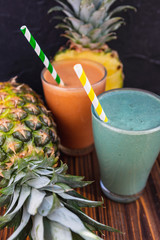 Blended green and orange smoothie with ingredients on wooden table