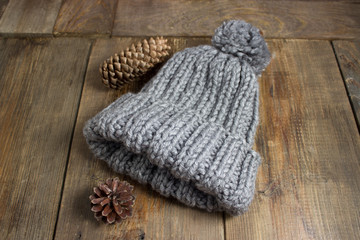 Fototapeta na wymiar Gray, knitted, winter, warm, soft handmade hat with a fir cone, on a brown background.