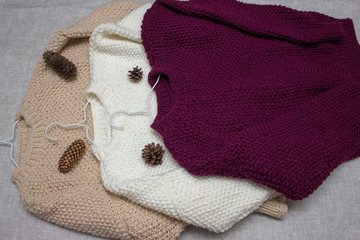 Pink, white, beige, knitted, warm, handmade winter sweater on gray background.