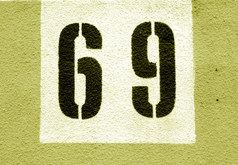 Number 69 on cement wall in stencil in yellow tone.