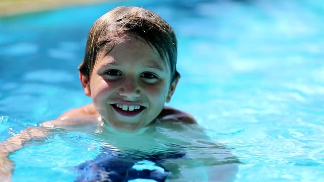 Kid inside swimming pool water smiling. Child boy portrait looking to camera during holidays summer vacations