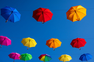 Fototapeta na wymiar Group of umbrellas hanging on a rope isolated against blue background, wallpaper background, bright various colors scenery