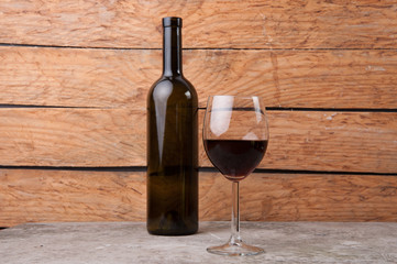 a bottle of wine, near a glass half filled with wine on wooden background