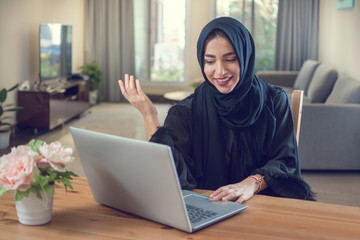 Smiling young arabian woman using laptop at home