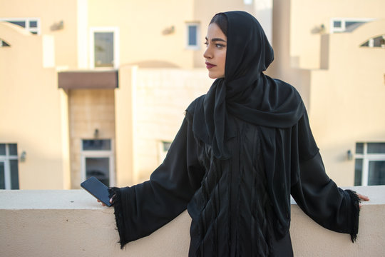 Beautiful Young Middle Eastern Woman Holding Smart Phone And Looking Over Balcony