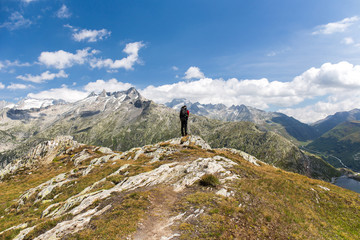 Hiker standing on the Alps mountain peak looking into the Grimsel valley, Switzerland