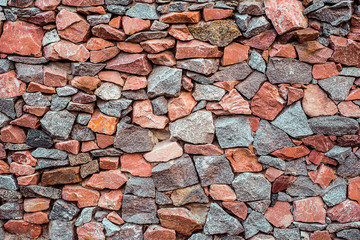 Stone wall texture from rocks of gray and red color, decorative uneven wall surface from real stone