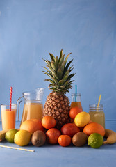 Fresh fruits with fruit juices on a blue background. Tasty composition of pineapple, mandarin, kiwi, Sicilian orange, lemon, lime and beverages. Exotic drink photography with copy space.