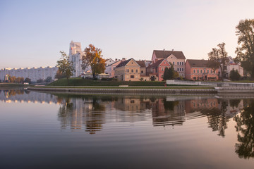 Fototapeta na wymiar Minsk, Belarus. Gentle dawn. Trinity suburb is reflected in the river Svisloch. Ducks swim in the river.