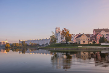 Fototapeta na wymiar Minsk, Belarus. Pink and lilac dawn. Buildings Trinity suburb and trees are reflected in the river Svisloch.