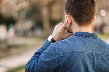 Back view of man usin wireless headphones. Man put his finger on headphone