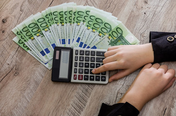 100 euro with a calculator and female hands on a wooden table