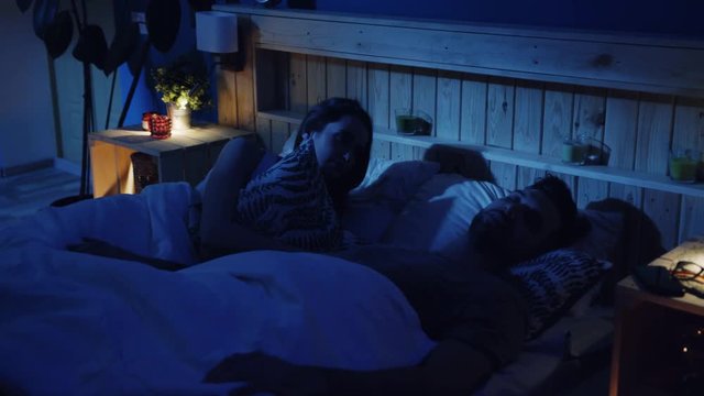 Young wife cannot sleep at night as her husband snoring beside her, woman turns away closing ears with a pillow. Irritation, tired, exhausted. Bad mood, negative emotions, problem. Health issue